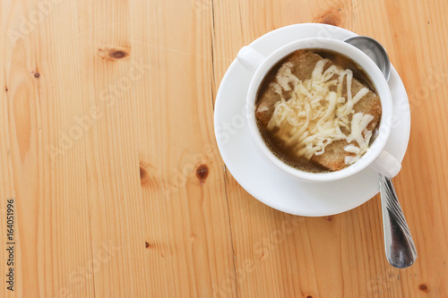 Onion soup on white ceramic bowl with hand on white dish and spoon on wood table texture