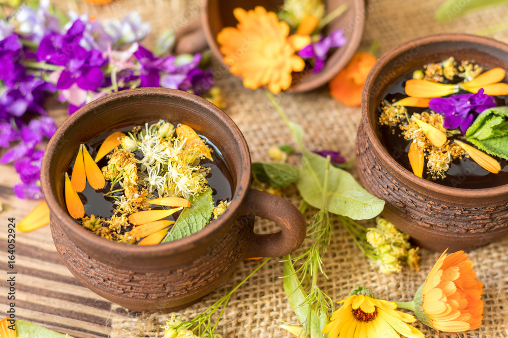 Two ceramic cups of healthy herbal tea with decoction of dry and fresh flowers on dark aged rustic wooden background. Shallow depth of field. Two ceramic cups of healthy herbal tea with decoction of dry and fresh flowers on dark aged rustic wooden background. Shallow depth of field.