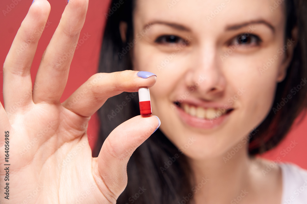 Beautiful young woman on a red background holds a pill Beautiful young woman on a red background holds a pill