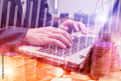 Double exposure stock financial on hand of businessman typing on laptop keyboard with coin stack. Financial stock market economy analysis. Business people and Economy financial concept.