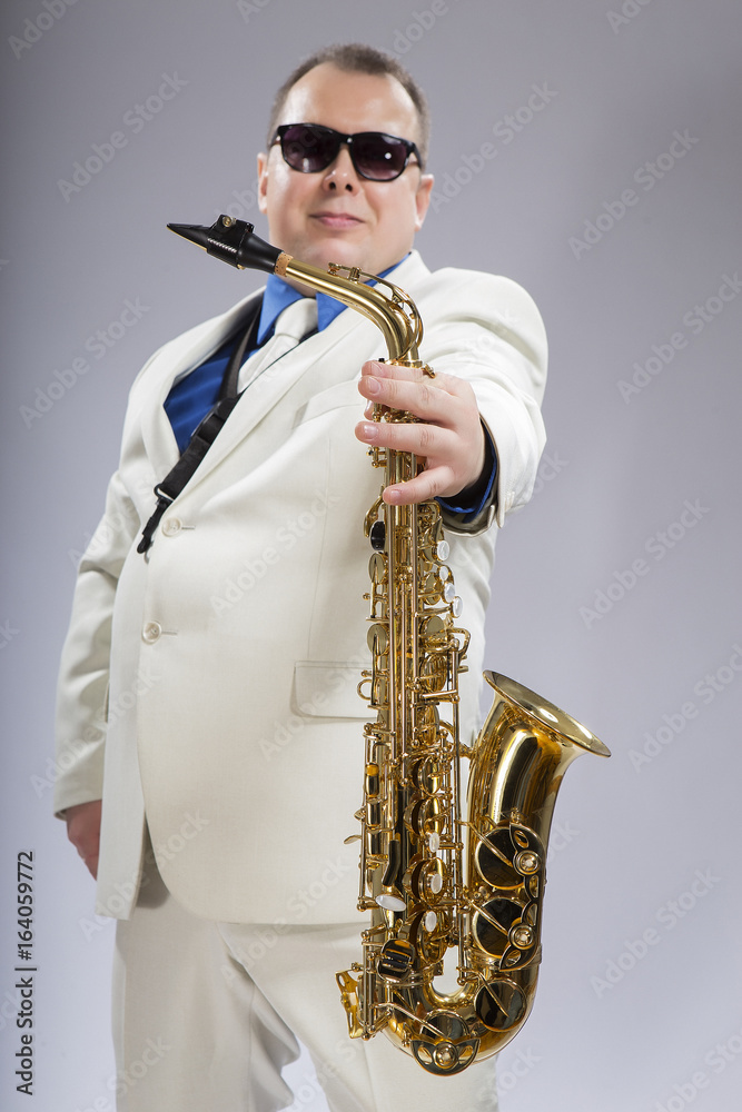 Fototapeta premium And you play. Saxophonist. Caucasian man with a saxophone. Dressed in a white suit. The studio silhouette on a white background.