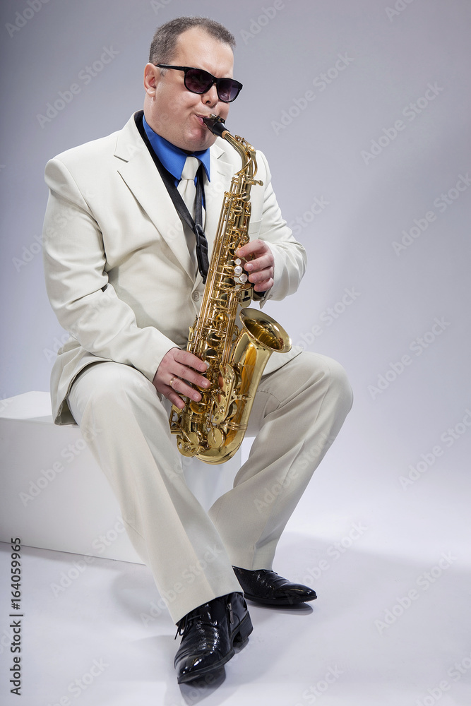 Fototapeta premium And you play. Saxophonist. Caucasian man with a saxophone. Dressed in a white suit. The studio silhouette on a white background.