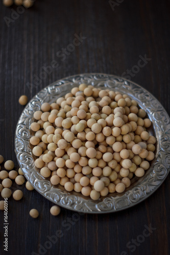 Soybeans in metal plate over black wooden background.