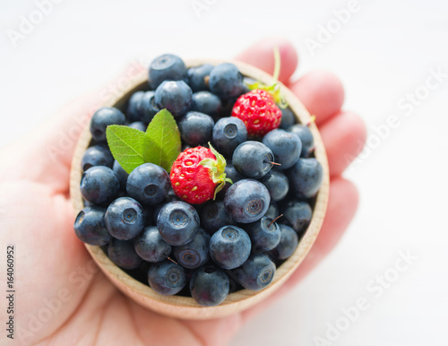 Fresh blueberries in a wooden cup on a female hand. Close up, top view.