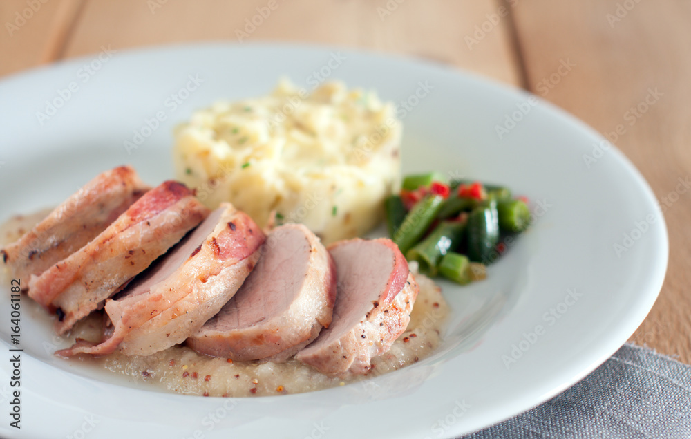 Pork tenderloin wrapped in bacon with pear and mustard puree, mashed potatoes and green beans with chilli