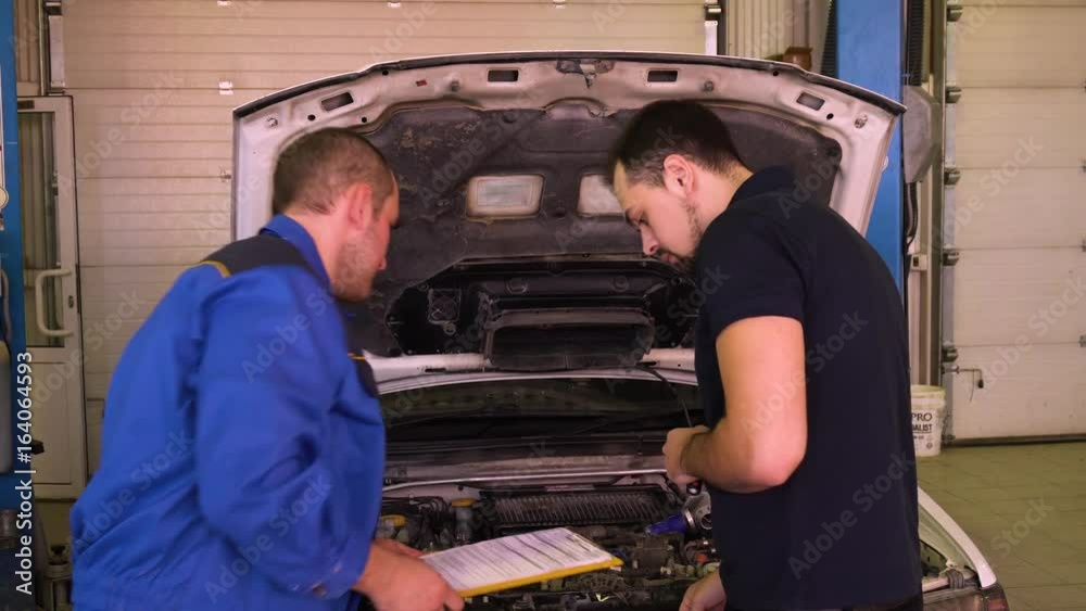 Auto mechanic tells the owner of the machine about the cost of repairs in garage. Auto mechanic tells the owner of the machine about the cost of repairs in garage.