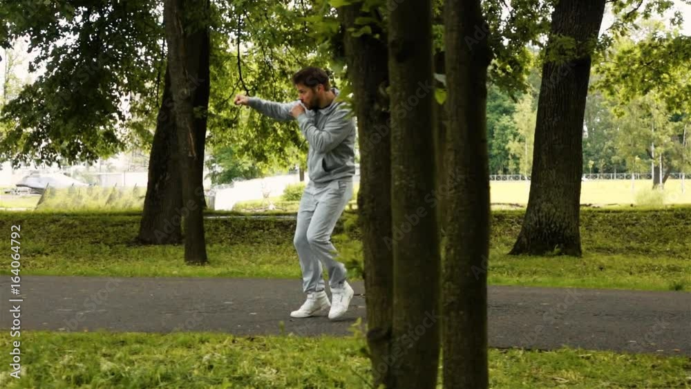 Young powerful Runner boxer in green park on asphalt road waving his arms with invisible enemy. Super slowmotion high-speed camera footage. Young powerful Runner boxer in green park on asphalt road waving his arms with invisible enemy. Super slowmotion high-speed camera footage.