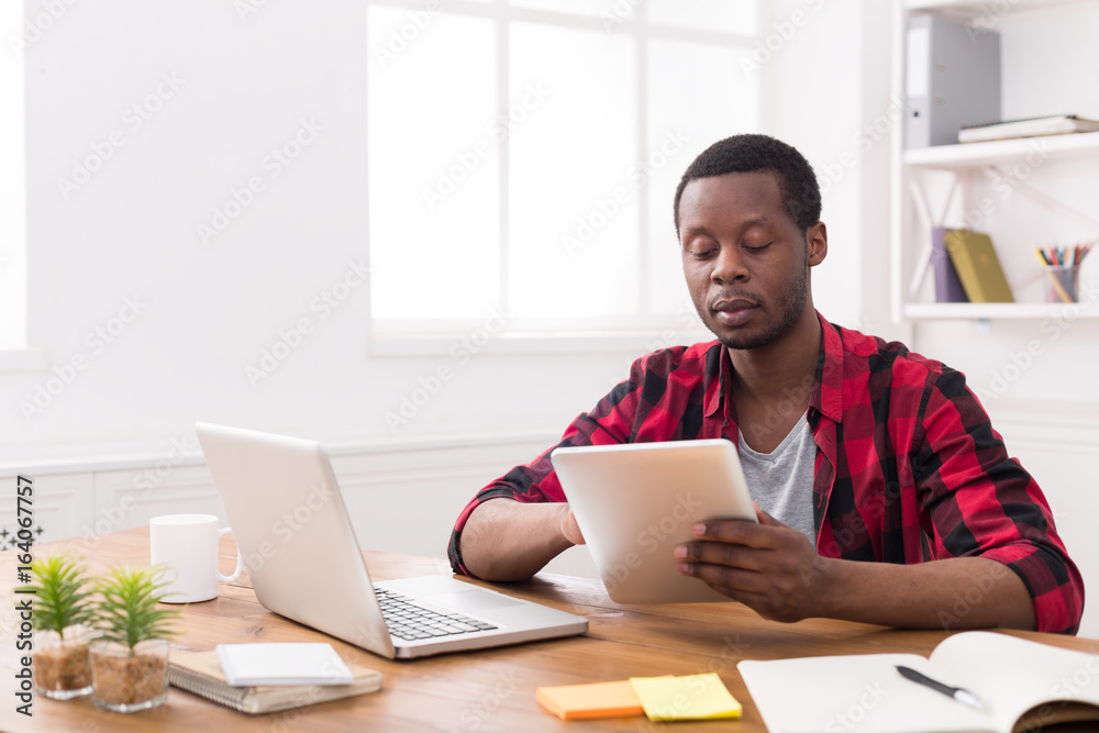 Black businessman in casual office, work both on laptop and tablet Black businessman in casual office, work both on laptop and tablet