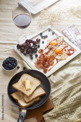English breakfast - fried egg, bacon, bread blueberry.and cherry in frying pan on wooden board over White tablecloth background