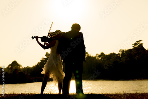 Woman playing violin and man listen music at the river on sunset,silhouette and blur photography. © somchaikhun