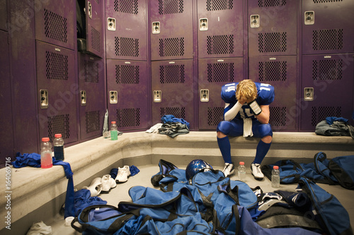 A Texas high school football player, the team's quarterback, in the locker room, head in hands, after losing their championship game.