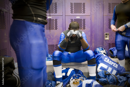 A football player sitting in a thoughtful state inside locker room