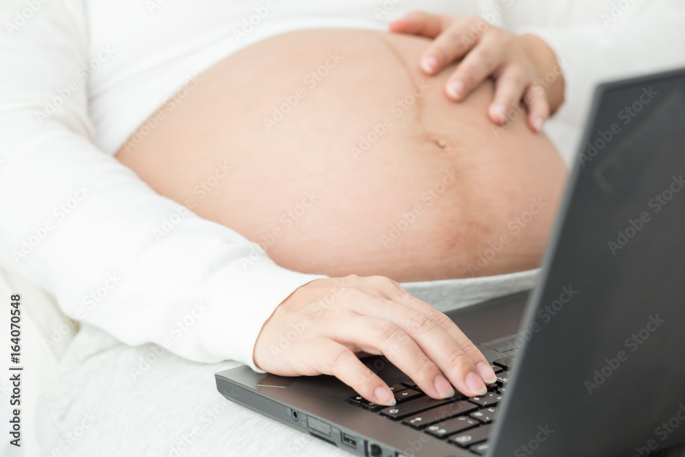 Naklejka premium Pregnant women working at home which online to head office by internet network and vpn to office with black laptop put on her leg