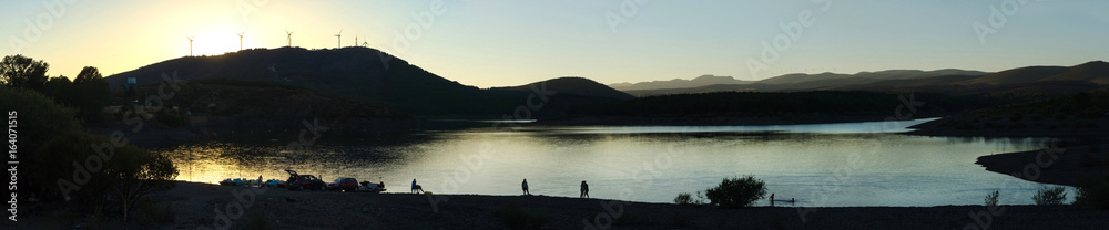 Gente a contraluz en un Atardecer en paisaje al lado de un Embalse o Lago al final del día de asueto Gente a contraluz en un Atardecer en paisaje al lado de un Embalse o Lago al final del día de asueto
