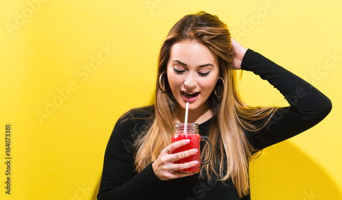 Happy young woman drinking smoothie on a yellow background