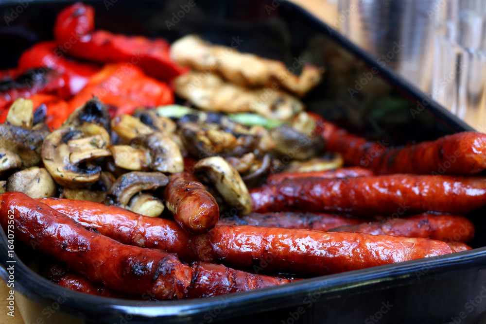 Grilled sausages, chicken breasts, edible mushrooms, zucchini and red pepper in a pan. Selective focus. Grilled sausages, chicken breasts, edible mushrooms, zucchini and red pepper in a pan. Selective focus.