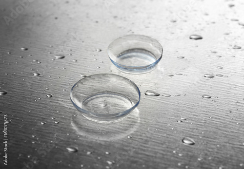 Contact lenses and drops of water on gray textured background