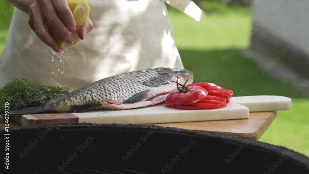 Raw carp is sprinkling with lemon juice in front of the fire of grill, preparations for the barbecue, cooking fish on the open fire, roasted fish, grill and barbecue, cooking outside