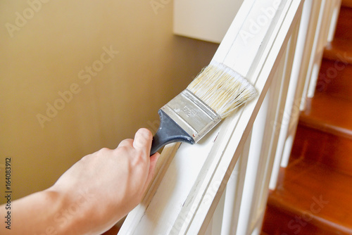 Hand Holding Paint Brush and Painting Stair Railings with White Color