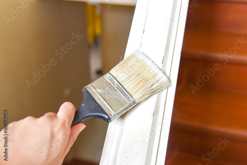 Close-Up View of Hand Holding Paint Brush and Painting Stair Railings with White Color