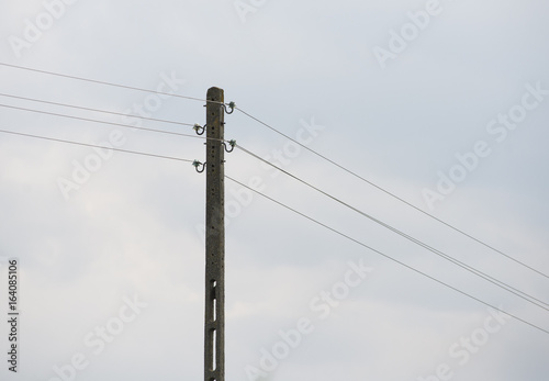 Słup elektryczny stojący na polu trzymający druty przewodzące prąd. Takie kable często padają łupem złodziei 
