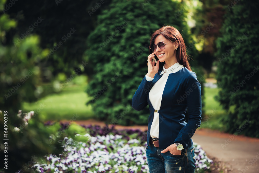 A business woman is talking on a mobile phone while walking at the city garden. A business woman is talking on a mobile phone while walking at the city garden.