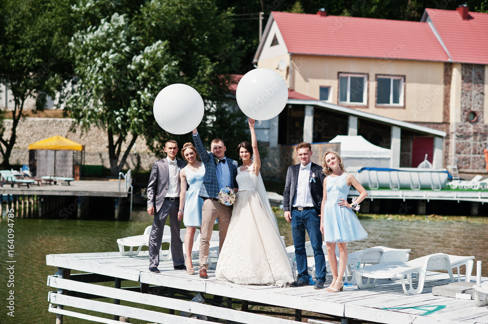 Fototapeta premium Wedding couple, groomsmen and bridesmaids having fun with balloons on wharf.