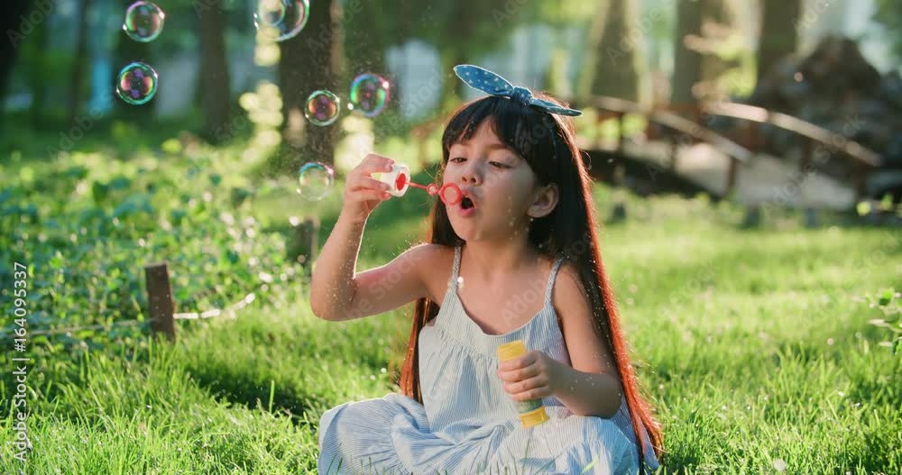 close-up of Happy little Asian girl blowing soap bubbles in spring Park. Slow motion