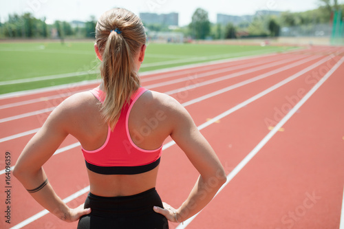 Young unrecognizable sporty woman athlete in sportswear ready to run on stadium track - back view
