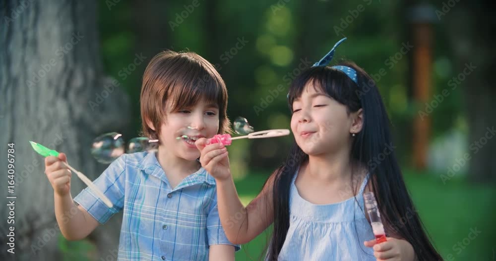 Happy children Caucasian boy and Asian girl blowing soap bubbles in spring Park, slow motion Happy children Caucasian boy and Asian girl blowing soap bubbles in spring Park, slow motion