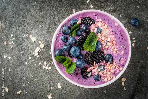 Ideas for healthy summer breakfast. Smoothie in bowl with blue (blueberry blackberries) berry With oatmeal, fresh berries. Dark stone table. Top view copy space