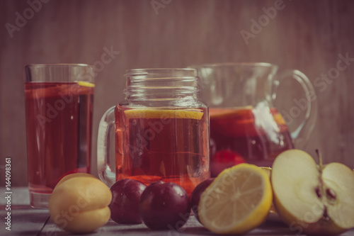 Homemade iced sweet tea with ripe apricots, plums and apples. Homemade tasty lemonade with fresh berries on a rustic wooden background