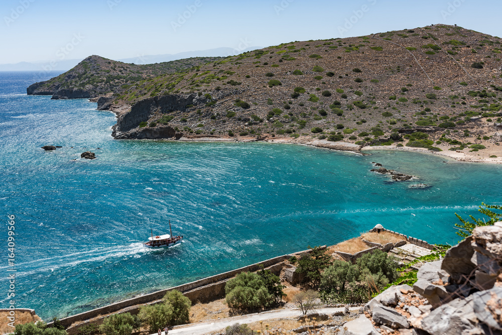 View from top of Spinalonga island. Blue sea with boat and Kalydon island in front.