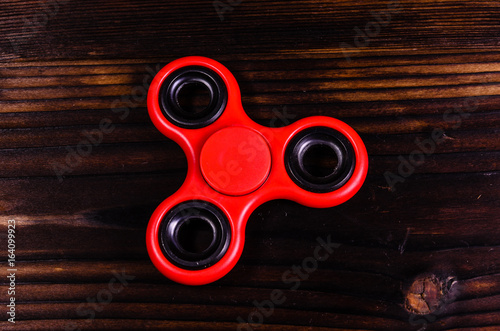 Red fidget spinner on wooden desk. Top view