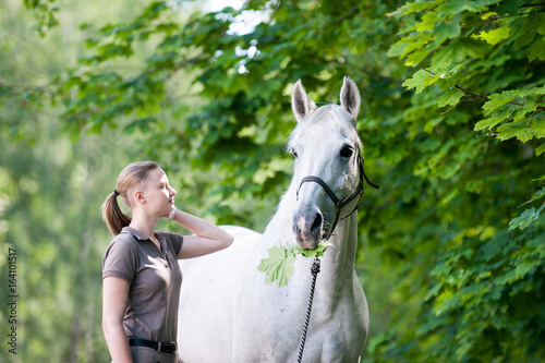 White horse with green maple tree leaves in mouth