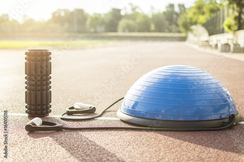 Close up of a bosu ball on a running track. Sport and fitness equipment. Foam roller for massage and pilates ball. Lens flare in the background.