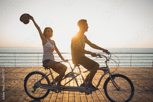 Obraz na płótnie Portrait of a mixed race couple riding on tandem bicycle outdoors near the sea