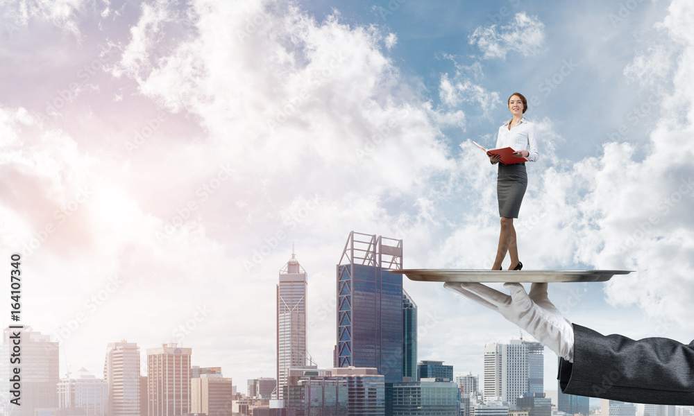 Attractive businesswoman on metal tray with red book in hands against cityscape background