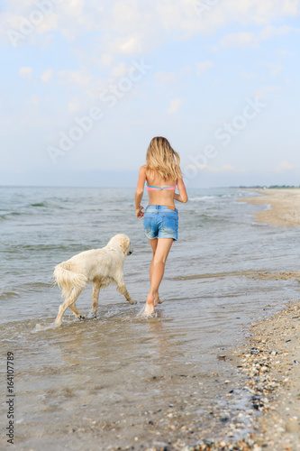 Teenage girl running along a beach shore with her golden retriever during the early morning.