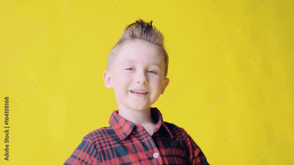 Portrait of happy smiling European blonde young boy with a modern fashion haircut, on yellow background, slow mo. Medium Close-Up. Cute little boy portrait, smiling to camera. Beautiful little child Portrait of happy smiling European blonde young boy with a modern fashion haircut, on yellow background, slow mo. Medium Close-Up. Cute little boy portrait, smiling to camera. Beautiful little child