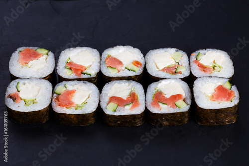 Delicious maki sushi roll with salmon,avocado and tofu cheese served on black slate, close up. Japanese food.