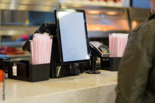Cash and order desk with order screen and card payment terminal with cashiers on back  in fast food restaurant
