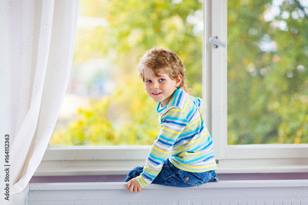 ittle kid boy sitting near window and looking on autumn trees ittle kid boy sitting near window and looking on autumn trees