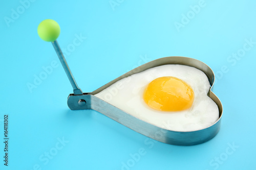 Fried sunny side up egg in heart shaped mold on color background