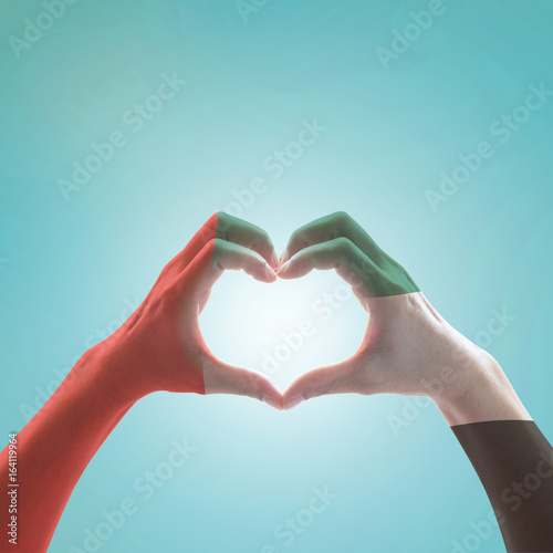 UAE  United Arab Emirate national flag pattern on people s hands in heart shape on blue mint sky background