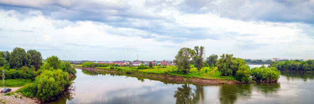 Landscape of a green forest and a small river with a mirror image of trees on a summer day, a blue sky with clouds, in the background a village Landscape of a green forest and a small river with a mirror image of trees on a summer day, a blue sky with clouds, in the background a village