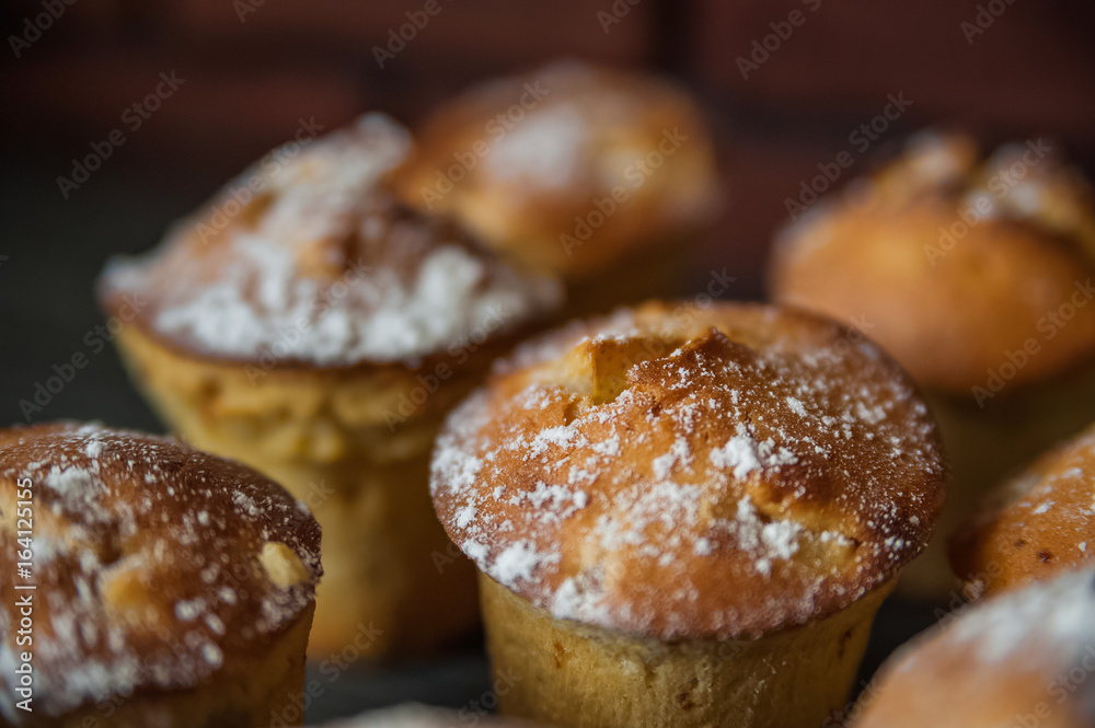 Fresh cooked cupcakes. Delicious homemade muffins with a pear. Cupcakes with a blue napkin on a dark black wooden table. Cupcakes, muffins sprinkled with powdered sugar on the background of a red bric