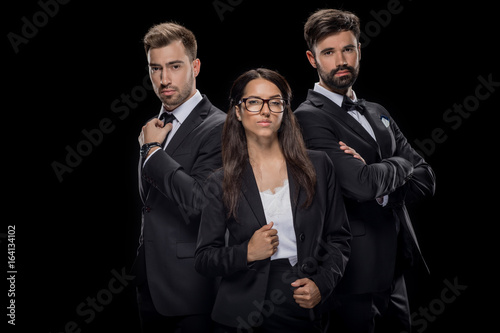 confident businesspeople posing in black formal wear, isolated on black