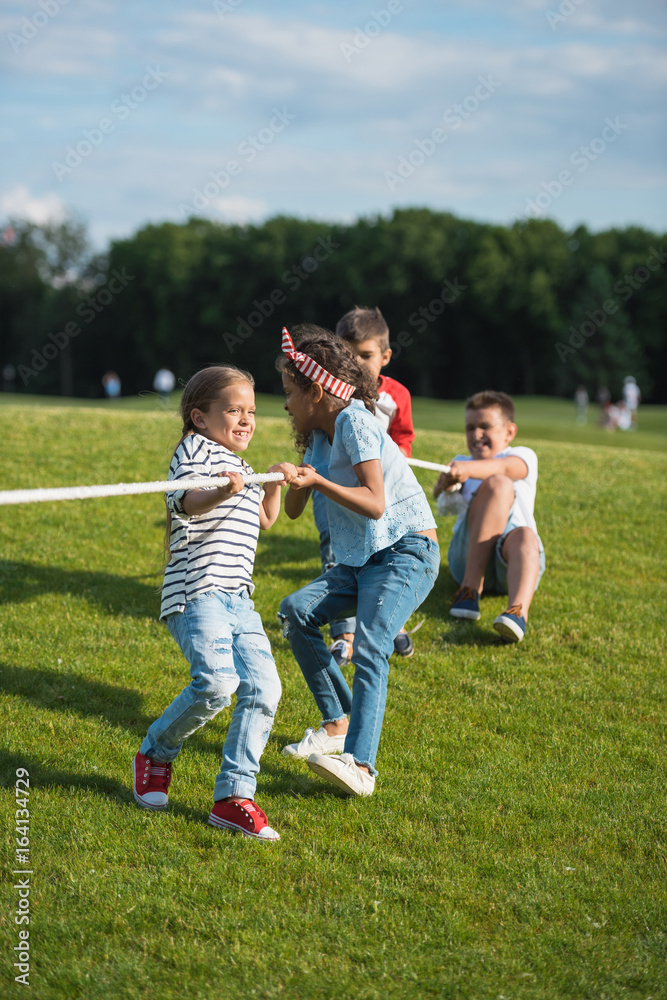 Multiethnic group of kids playing tug of war on green grass in park Multiethnic group of kids playing tug of war on green grass in park