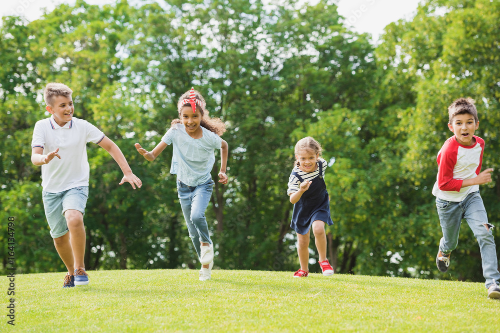 Adorable happy multiethnic kids playing and running together on green grass in park Adorable happy multiethnic kids playing and running together on green grass in park